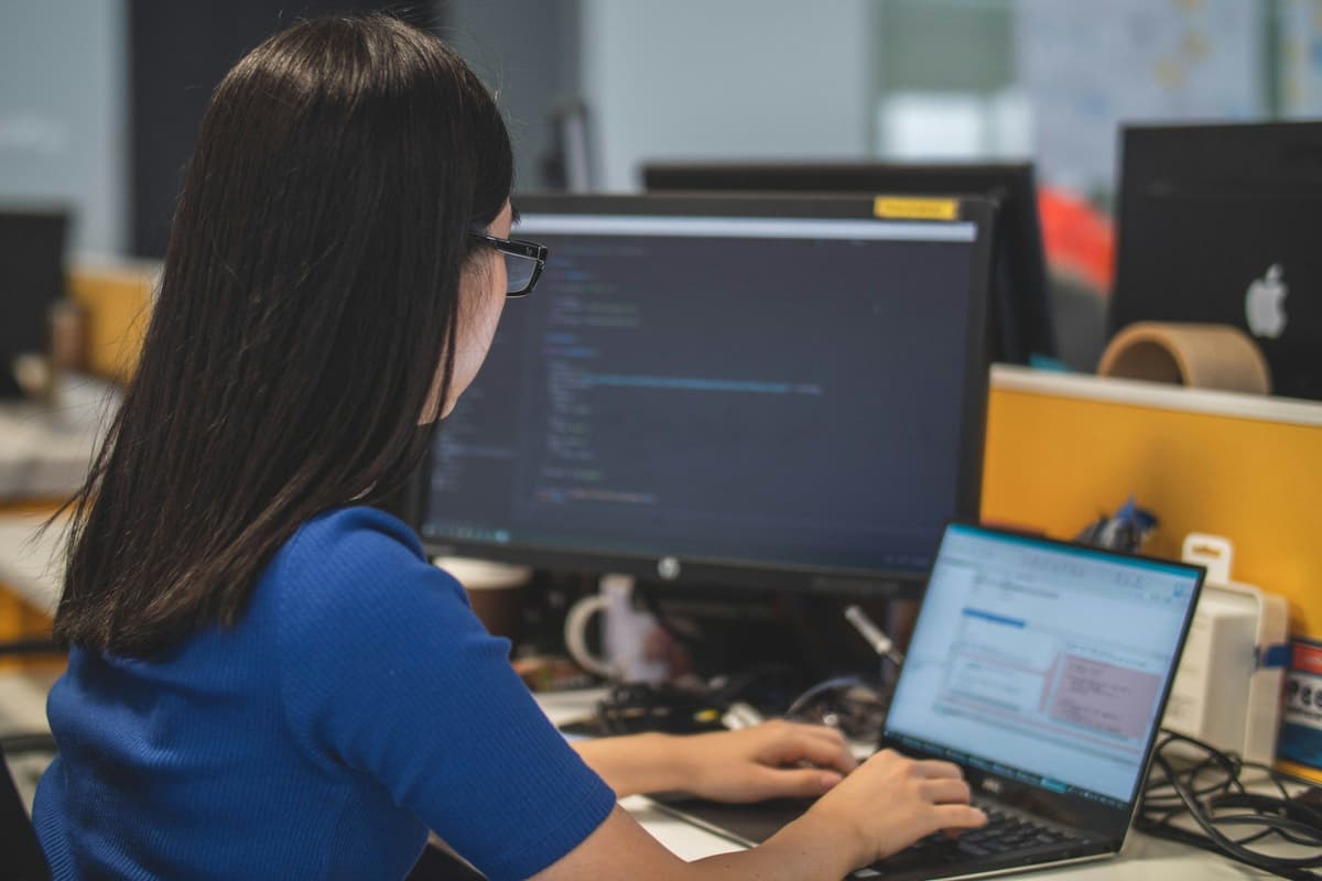woman using black laptop computer near turned on flat screen computer monitor